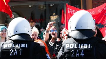 Vastamielenosoittaja näyttää keskisormea. Etualalla on poliisien selkiä.