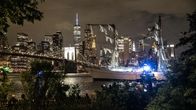 Ett segelfartyg med skadade master och rigg avtecknar sig mot Manhattans skyline i kvällsbelysning.