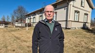 Henkilö seisoo puisen asuinrakennuksen edustalla.