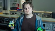 Taitaja-finalisti Miro Patrikainen katsoo kameraan ja pitelee käsissään kahta rakentamaansa robottia.