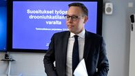 Bilden visar en man med glasögon, papper i handen vid ett presstillfälle.