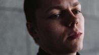 Kuvassa henkilö seisoo harmaata seinää vasten.