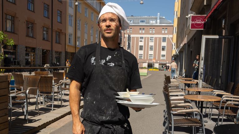 Mies kokin asussa kädessään lautasia. 