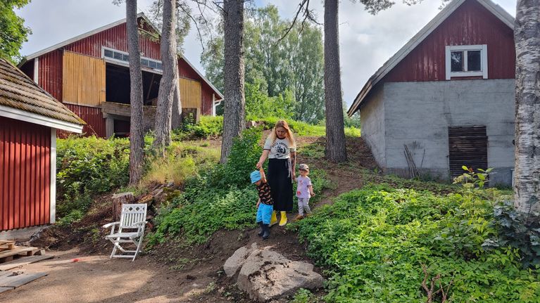 Äiti ja kaksi pientä lasta laskeutuvat rantatörmää alas.