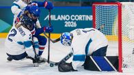 Hockeymålvakt i vitt försöker få tag på en puck som ligger på isen.