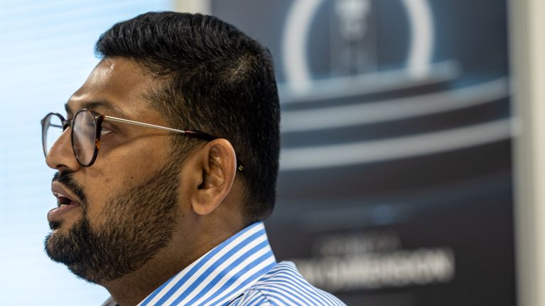 Profilfoto av en person i en randig skjorta som sitter i kontorsmiljö framför en mörk affisch.