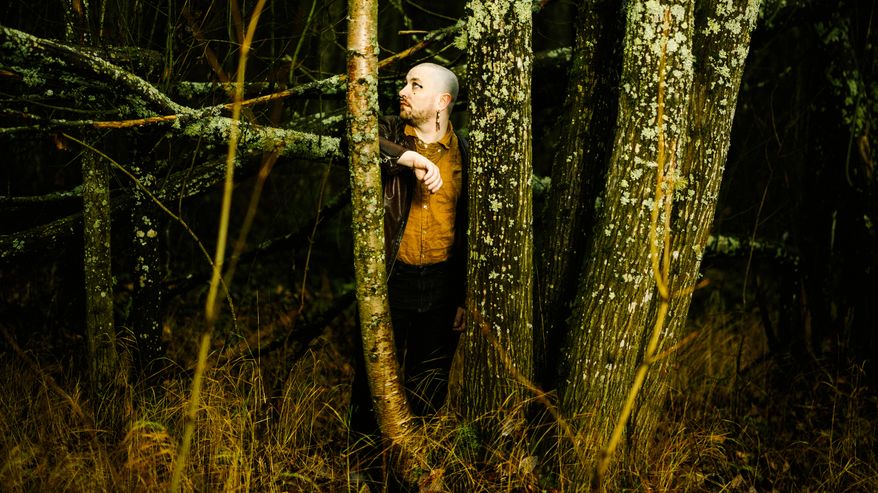 Henkilö seisoo syksyisessä metsässä yllään ruskea nahkatakki.
