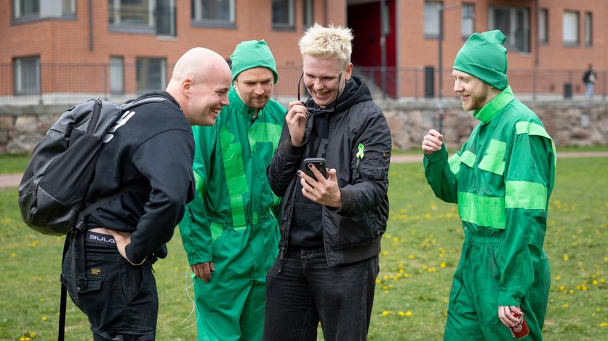 Neljä miestä nauraa puhelimesta näkyvälle videolle.