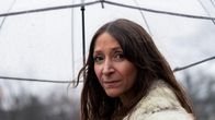 Kuvassa henkilö pitää kirkasta sateenvarjoa yllään turkisvaate, sateinen ja harmaa päivä.