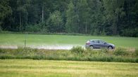 Henkilöauto ajaa sateisella tiellä peltojen keskellä.