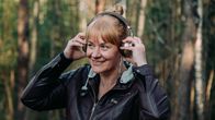 Nainen kuuntelee kuulokkeilla ulkoilmassa. 