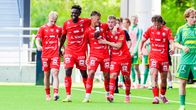 Fem fotbollsspelare i röda matchställ med texten "A. Wiklöf" på tröjorna går tillsammans på en gräsplan.
