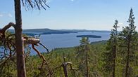 Etualalla näkyy korkeata kalliota, alhaalla avautuu järvimaisema saarineen.