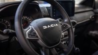 Dacia-henkilöauton ohjauspyörä ja kojelauta, taustalla mittaristo ja keskikonsolin näyttö.