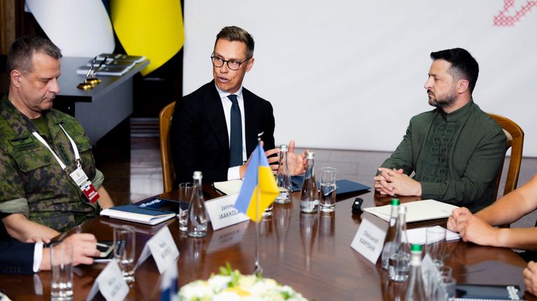 Neljä henkilöä neuvottelupöydän ääressä Ukrainan ja Euroopan unionin liput pöydällä, asiakirjoja ja juomalaseja.