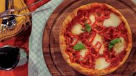 Pizza tarjoiltuna pyöreällä puualustalla, koristeltuna paprikasiivuilla, sulalla juustolla ja tuoreilla basilikanlehdillä.