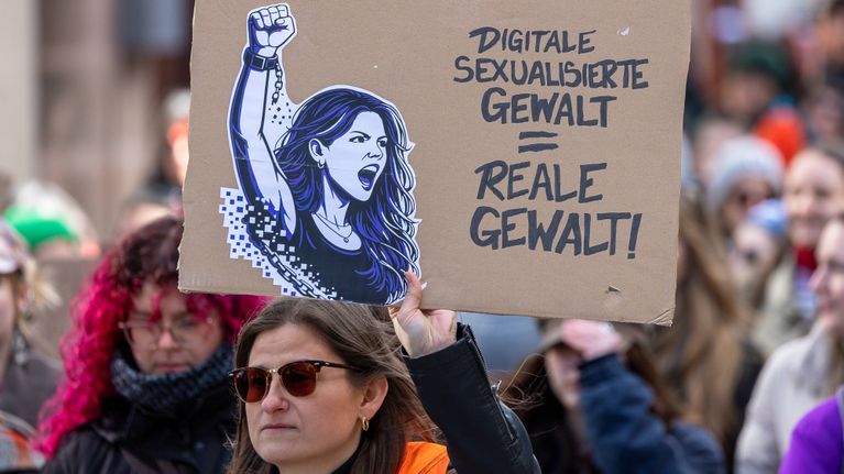 Vakavan ilmeen omaava osallistuja pitää kädessään mielenosoituskylttiä, jossa lukee Digitaalinen seksuaalinen väkivalta = todellista väkivaltaa.