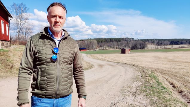 Tomas Gripenberg står vid en åker där det kör en traktor långt i bakgrunden.