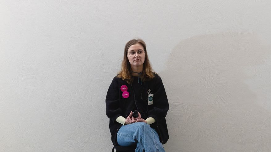 Museovalvoja Minna Arponen istuu vahtipaikallaan. Taustana valkoinen seinä.