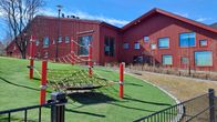 En lekpark framför ett rött skolhus.