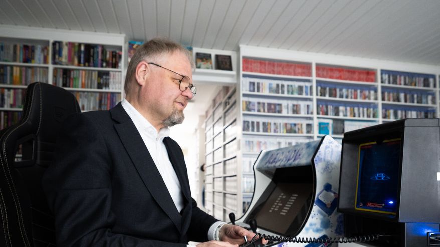 Mika Hoffrén istuu työpöydän ääressä ja pelaa videopeliä pelikokoelmansa keskellä.