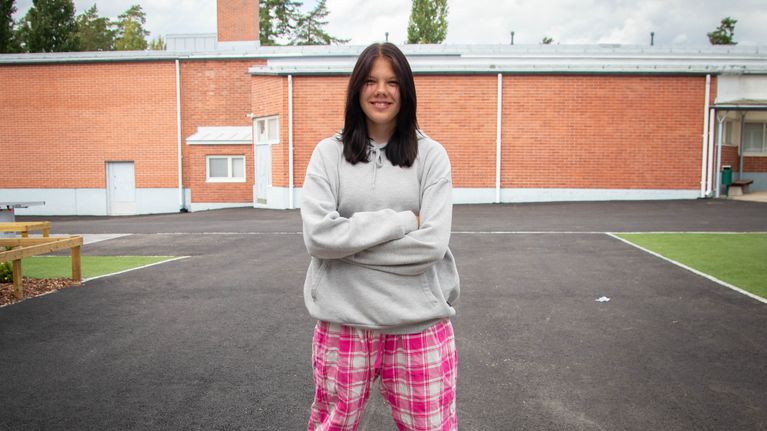 Seiskaluokkalainen Minttu Huhtinen seisoo koulun pihalla pinkit pyjamahousut yllään ja hymyilee kameralle.