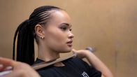 Sofia Rönkkö kokeilee painonnostotangon asentoa ilman painoja. Hänen pitkät mustat hiuksensa on letitetty kymmenille leteille. 