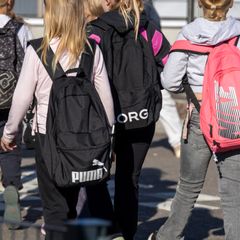 Useita koululaisia kävelee koulun pihalla reppujen kanssa.