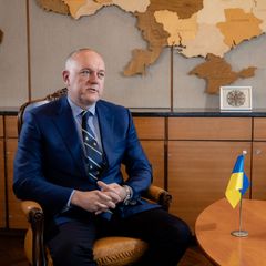 Ukraine’s ambassador to Finland, Mykhailo Vydoinyk, sitting in a chair at the Ukrainian embassy. On the table there is a Ukrainian and Finnish flag.