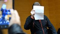 Seisomassa oleva syytetty peittää kasvojaan oikeudessa paperilapulla.