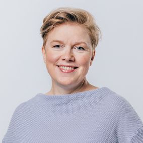 Kuvassa Terhi Vuorinen pukeutuneena vaaleansiniseen neulepaitaan, seisoo neutraalin vaalealla taustalla.