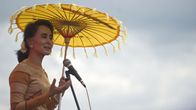 Aung San Suu Kyi pitää puhetta keltainen päivänvarjo pään päällä.