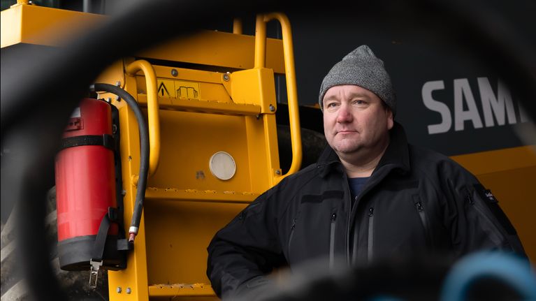 Maatalousyrittäjä Anssi Mennala seisoo katoksessa leikkuupuimurinsa luona. 