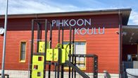 Punainen hirrestä rakennettu koulu jonka edessä on lasten leikkiteline. 