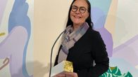 Tummahiuksinen, silmälasipäinen museonjohtaja Tuulia Tuomi hymyilee ja pitää käsissään valkoista kipsipystiä, jossa on kullattu yläosa.