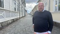 Mies seisoo nupulakivetyllä kadulla. Hänen ilmeensä on neutraali.