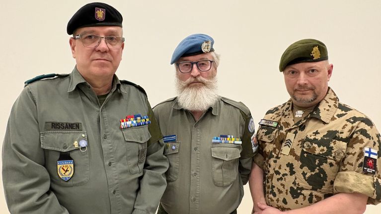 Kuvassa kolme miestä, joilla kaikilla on baretit päässään. Vaatteissa on erilaisia sotilastunnuksia.