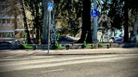 Fyra elsparkcyklar står vid en trottoar intill träd, med skyltar för övergångsställe och gång- och cykelväg.