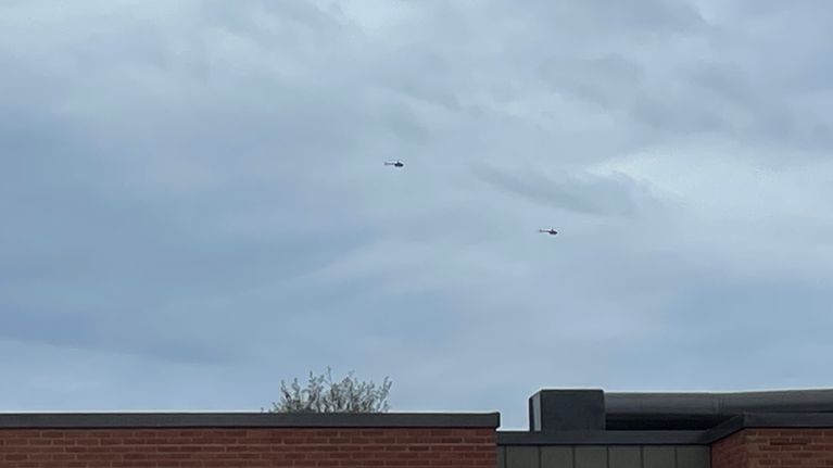 Kaksi helikopteria lentää peräkkäin kauemmpana. Etualla tiilimuuri.