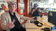 Kaksi henkilöä keskustelee studiossa äänityslaitteiden äärellä toimistoympäristössä.