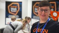 Josefin Stolpe i en "Energy Week"-tröja. I bakgrunden finns affischer och människor som verkar delta i ett evenemang eller en aktivitet.