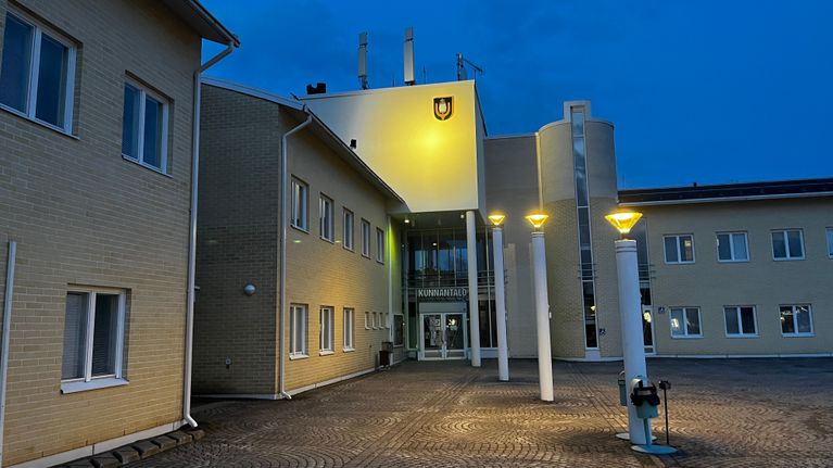 Valaistu vaaleankeltainen suuri rakennus, jonka oven yläpuolella lukee "Kunnantalo". 