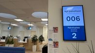 Toimisto, jonka seinällä on iso näyttö. Näytällä lukee Nyt palvellaan 006 ja palvelupiste 2.
