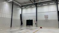 En avlång inomhushall med högt i tak, en basketkorg på väggen och utrustning på golvet.