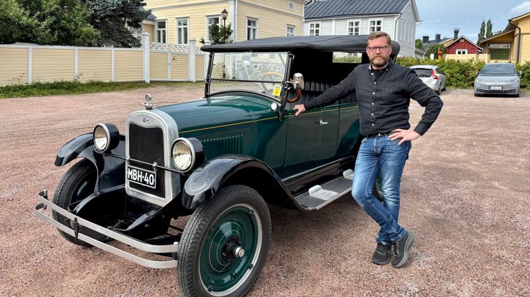 En man står bredvid en gammal bil.