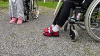 Vaaleanpunaiset Reino-tossut, omistaja istuu pyörätuolissa