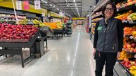 Myyjä seisoo kaupan hedelmäosastolla ja katsoo hymyillen kameraan.
