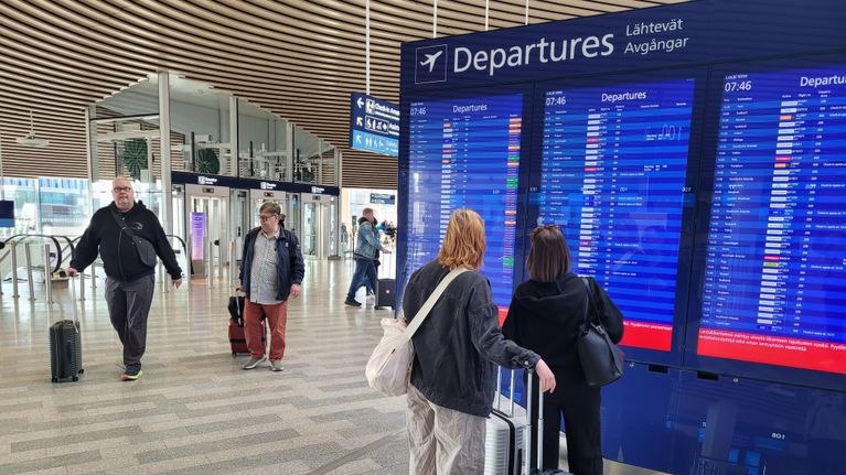 Matkustajat odottavat lentojen lähtöauloissa seuraten lähtötaulun tietoja lentoasemalla.