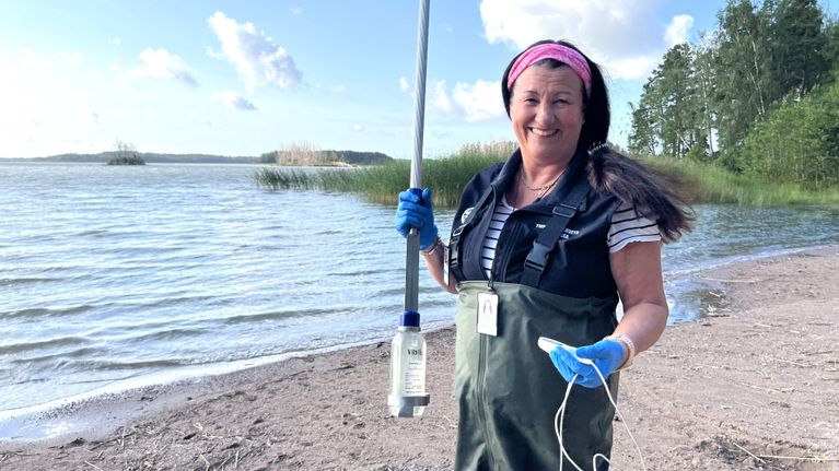 En kvinna står vid vattenbrynet iklädd vadarbyxor.
