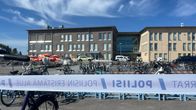 koulun edustalla on poliisin eristämä alue. Kuvassa näkyy poliisin sininen teippi, joka estää pääsyn eristetyille alueille. Taustalla näkyy koulun rakennuksia ja useita poliisiautoja.